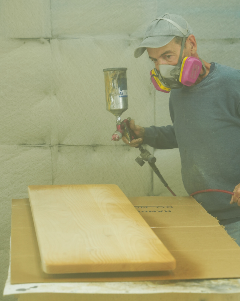 Craftsperson spraying a clear finish onto the bench top in the spray booth