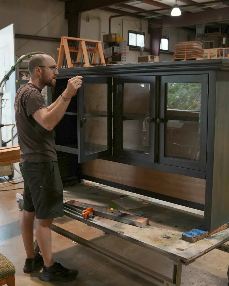 G. Michael's furniture restorer inspecting a refinished cabinet in the Fort Collins workshop